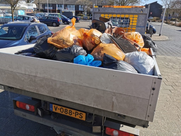 Een auto met open laadbak met volle vuilniszakken en zwerfvuil